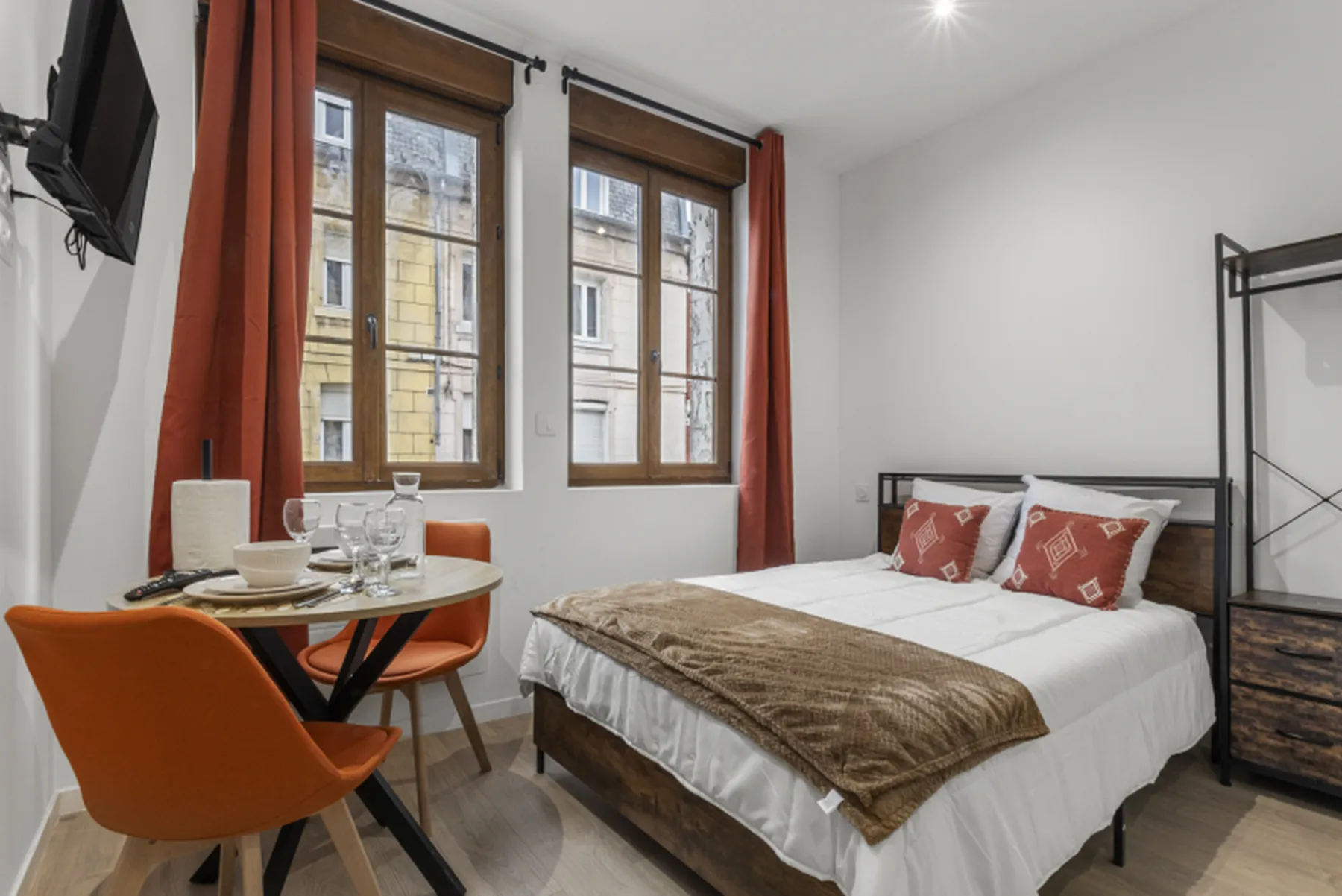 Studio Terracotta : coin repas aux chaises orange et lit double, sous une grande fenêtre donnant sur les toits de Saint-Quentin